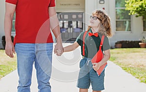 Portrait of happy nerd pupil holding teachers hand. American father and son walking trough school park.