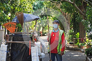 Portrait happy old Asian man street cleaner standing next to an old gabage cart before going to work with nature background