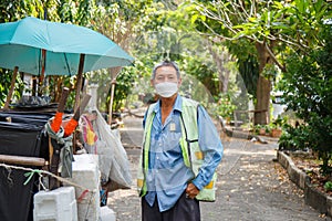 Portrait happy old Asian man street cleaner wearing a masks pick a pocket next to an old garbage cart before going to work with
