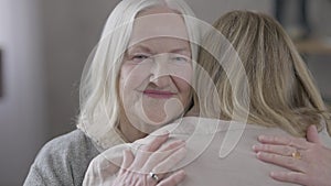 Portrait of happy old Caucasian mother hugging daughter at home indoors looking at camera. Close-up of smiling calm