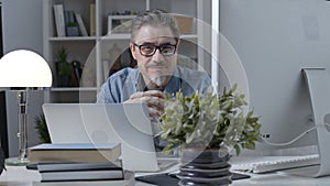 Portrait of happy older man in glasses at desk at home