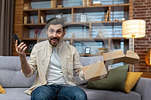 Portrait of happy online shopper at home, mature adult man smiling and looking at camera, holding product box and phone
