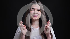 Portrait of happy overweight brunette caucasian girl gesturing crossed-fingers sign to show hope into camera on black