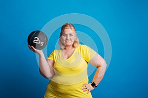 Portrait of a happy overweight woman holding a heavy ball in studio.