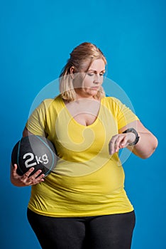 Portrait of a happy overweight woman with smartwatch and heavy ball in studio.