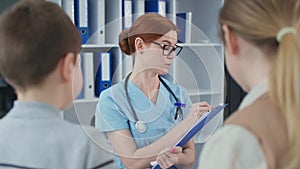 portrait of happy physician in blue uniform in hospital office, family doctor writes a prescription for the patient's