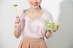 Portrait of a happy playful girl eating fresh salad from a bowl and winking isolated over white background