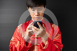 Portrait of happy positive handsome young Asian business man in red Chinese clothes, Qipao or Cheongsam is smiling, using