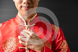 Portrait of happy positive young Asian business man in red Chinese clothes, Qipao or Cheongsam is smiling, touching clothes like