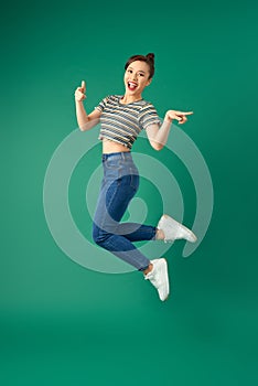 Portrait of happy positive young Asian woman jumping and waving hand over green background