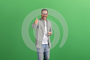 Portrait of happy positive young man smiling and showing thumbs up sign on isolated green background