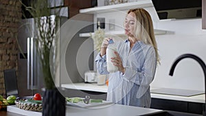 Portrait of happy pregnant Caucasian woman smelling milk smiling standing in kitchen at home. Joyful beautiful expectant