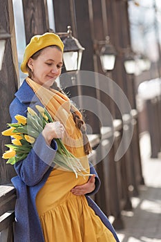 Portrait of a happy pregnant woman with a bouquet of yellow tulips on a walk in spring.