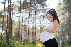 Portrait of happy pregnant woman outdoors in nature, touching her belly.