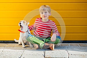 Portrait of happy preteen boy playing holding on hands with his dog Jack Russell Terrier on yellow background outdoor. Friendship