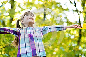Portrait of happy pretty child girl having fun in autumn forest. Positive female kid enjoying warm day in fall park