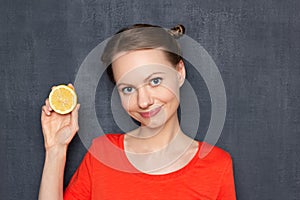 Portrait of happy pretty girl holding half of lemon and smiling