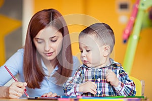 Portrait of happy pretty mother with her toddler son drawing