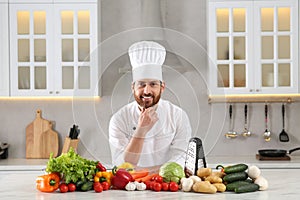 Portrait of happy professional chef near vegetables at marble table in kitchen