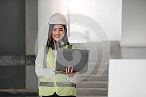 Portrait of Happy professional construction engineer woman holding laptop and wearing the safety helmet at the building