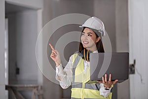 Portrait of Happy professional construction engineer woman holding laptop and wearing the safety helmet at the building