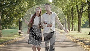 Portrait of happy relaxed young couple strolling in sunny summer park. Beautiful young Caucasian woman and handsome man