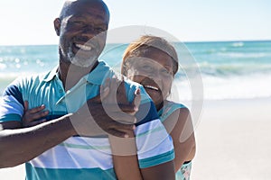 Portrait of happy retired african american senior couple standing together at beach on sunny day