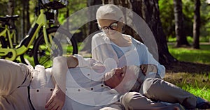 Portrait of happy retired couple relaxing on grass in summer park
