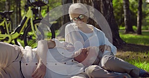 Portrait of happy retired couple relaxing on grass in summer park