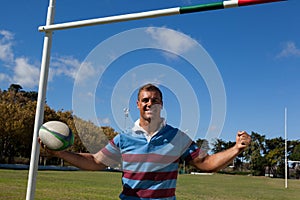 Portrait of happy rugby player holding ball against blue sky