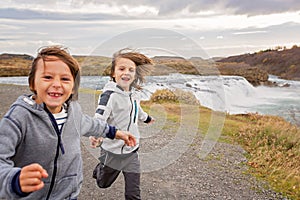 Portrait of happy running kids, boy brothers, near smaller waterfall around Gullfoss, Iceland