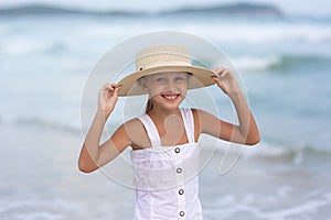 Portrait of a happy Russian little girl in a white dress and hat on a background of the sea. The child walks in the fresh air.