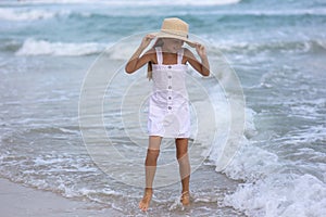 Portrait of a happy Russian little girl in a white dress and hat on a background of the sea. The child walks in the fresh air.