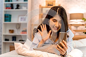 Portrait of happy 20s aged Asian woman in casual clothing making facetime video calling with smartphone at home. She`s