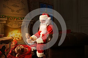 Portrait of happy Santa Claus sitting at his room at home near Christmas tree and reading Christmas letter or wish list.