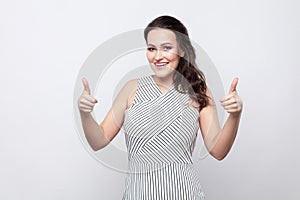 Portrait of happy satisfied beautiful young brunette woman with makeup and striped dress standing, toothy smiling and looking at