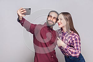 Portrait of happy satisfied couple standing, looking and smiling at camera of mobile smart phone to make selfie or video call with