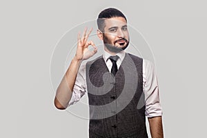 Portrait of happy satisfied handsome bearded brunette man in white shirt and waistcoat standing looking at camera and smiling and