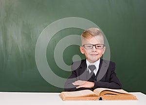 Portrait of a happy schoolboy with book near empty green chalkboard