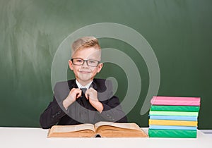 Portrait of a happy schoolboy in a suit near empty green chalkboard