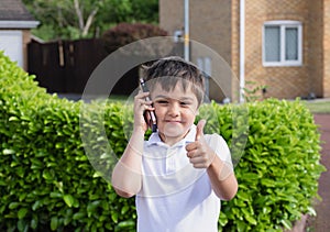 Portrait Happy schoolboy talking on mobile phone with friend. Cute Child using smart phone while standing outsid waiting for