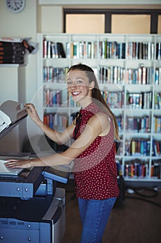 Portrait of happy schoolgirl using Xerox photocopier in library