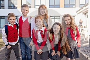 Portrait of happy schoolkids in uniforms with teacher at schoolyard, looking at camera.