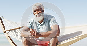 Portrait of happy senior african american man sitting in hammock on sunny beach