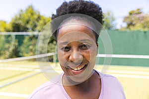 Portrait of happy senior african american woman smiling on sunny grass tennis court
