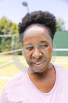 Portrait of happy senior african american woman smiling on sunny grass tennis court