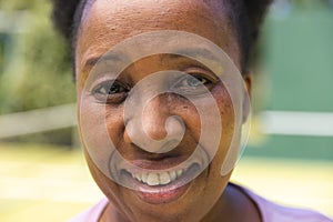 Portrait of happy senior african american woman smiling on sunny grass tennis court