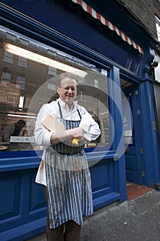 Portrait of a happy senior butcher standing outside shop with cleaver