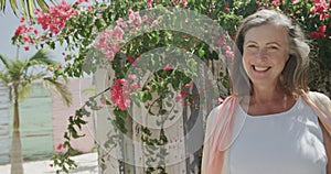 Portrait of happy senior caucasian woman smiling in the sun by pink flowers, in slow motion