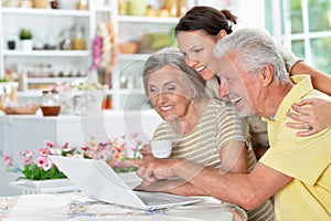 Portrait of happy senior couple with adult daughter using laptop at home, online shopping concept